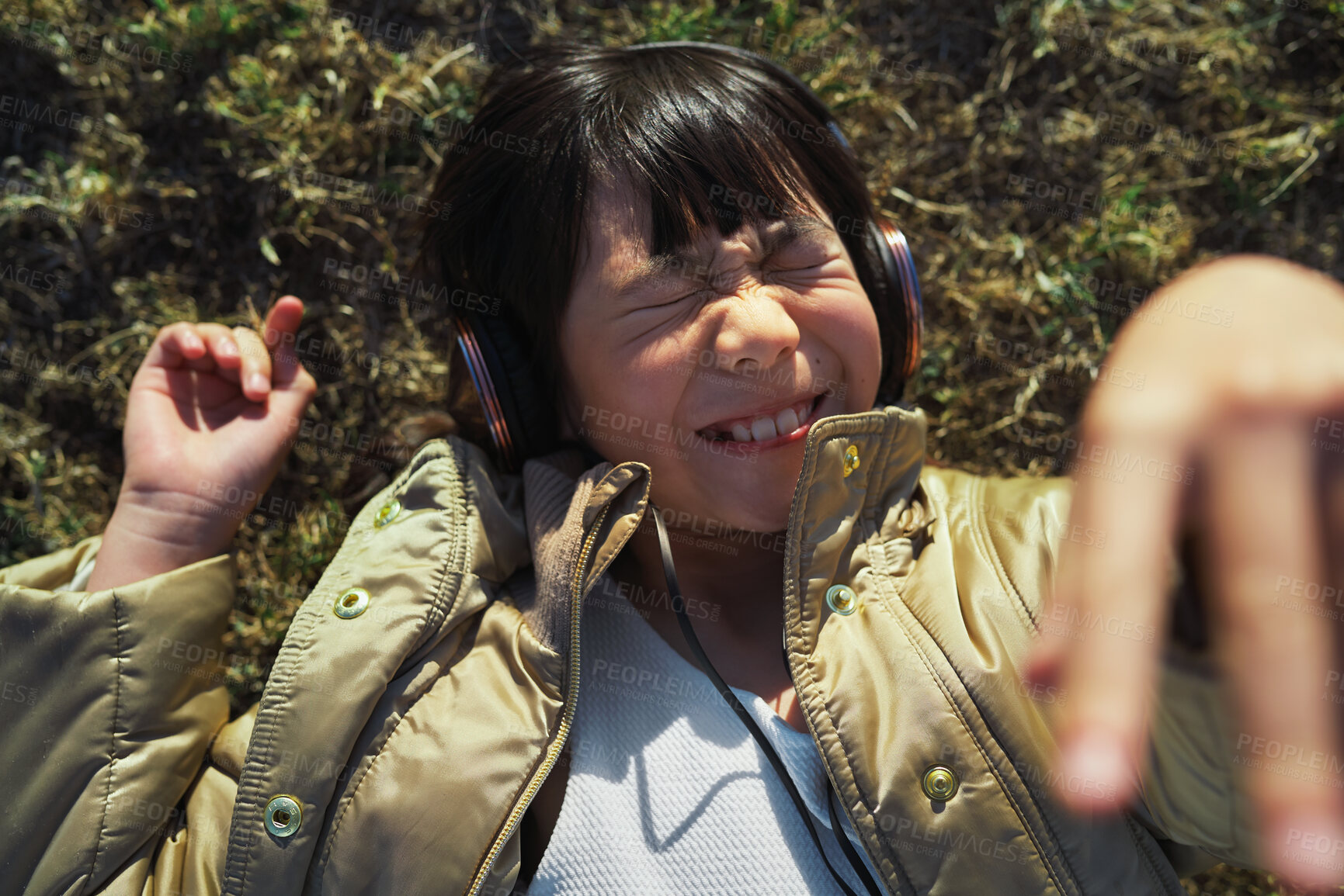 Buy stock photo Funny, playful and girl with headphones on grass for freedom, comedy and crazy in Singapore. Summer, comic and Asian child lying in park to relax, streaming music and lisrening to audio while playing