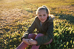 Beautiful little girl sitting on grass in park at sunset