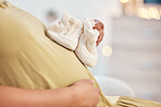 Black woman, pregnancy stomach and closeup of shoes on home living room sofa, hands and excited for baby. Future mother relax, couch and pregnant in lounge by blurred background in house with hope