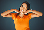 Woman, hands on face and smile portrait in studio for kindness, beauty and motivation for happiness. Model person with orange t-shirt for fashion, happy mindset and mental health on a blue background