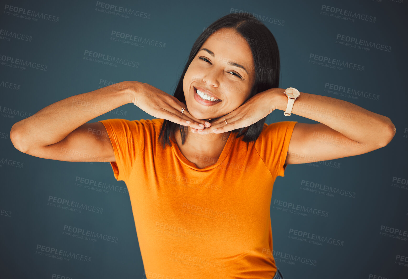 Buy stock photo Woman, hands on face and smile portrait in studio for kindness, beauty and motivation for happiness. Model person with orange t-shirt for fashion, happy mindset and mental health on a blue background