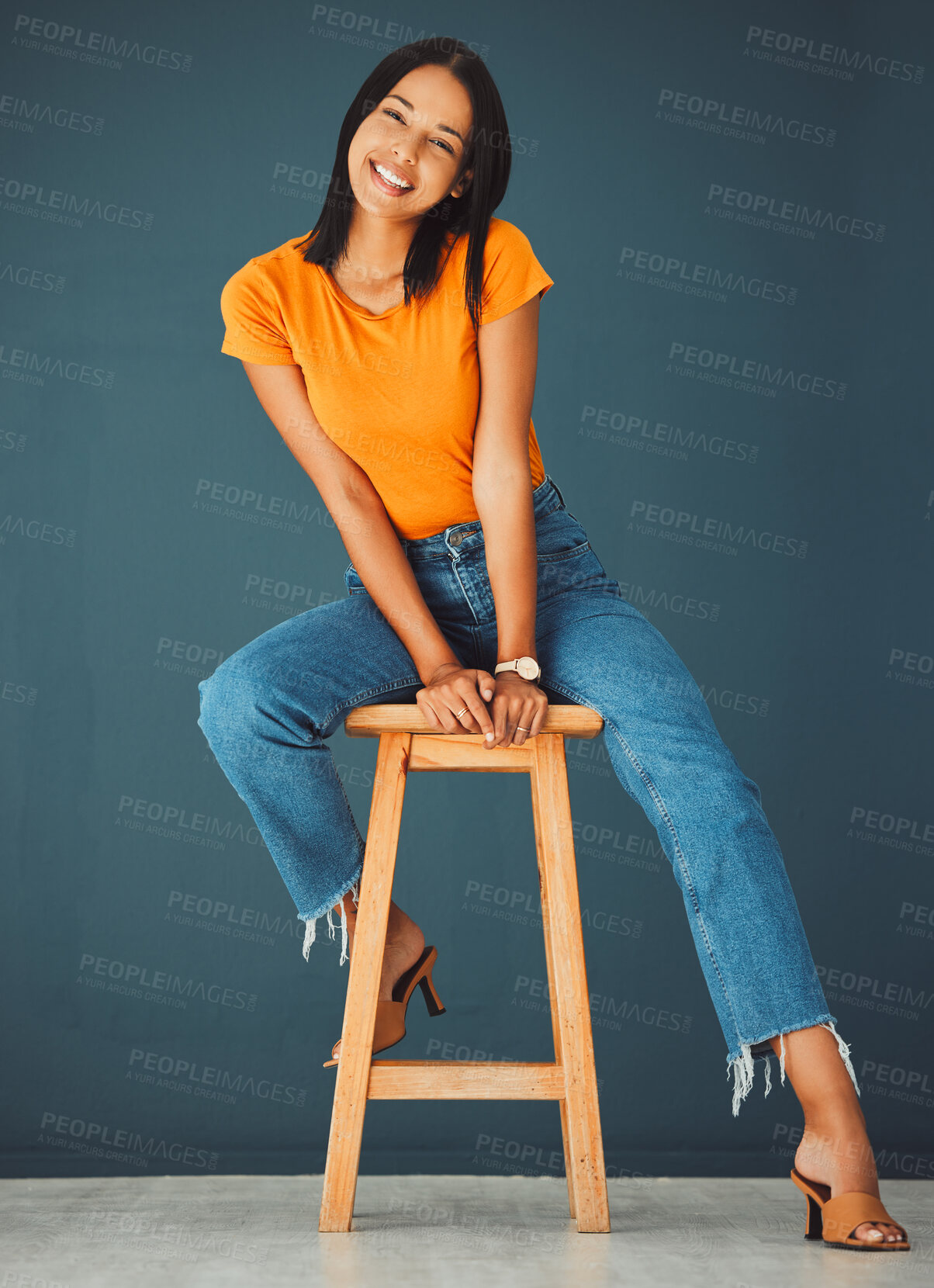 Buy stock photo Black woman, smile and portrait of a young model sitting on a stool in a studio. Casual fashion, happiness and youth of a female feeling relax, calm and happy on a chair isolated by a blue wall