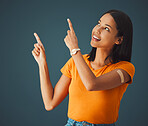 Woman, hands and pointing in studio for covid, vaccine and healthcare with mockup, space and grey background. Health, girl and model with plaster for corona, shot and immunity or isolated copy space