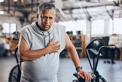 Sports, gym and senior man with pain in chest, medical emergency during workout at fitness studio. Health, wellness and inflammation, old man with hand on heart cramps while training on exercise bike