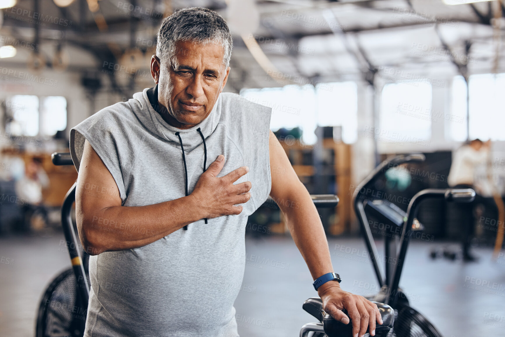 Buy stock photo Gym, pain in chest and senior man with medical emergency during sports workout at fitness studio. Health, wellness and inflammation, old man with hand on heart attack while training on exercise bike.
