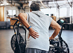 Sports, gym and injury, old man with back pain, emergency during workout at fitness studio. Health, wellness and inflammation, senior person with hand on muscle cramps while training on exercise bike