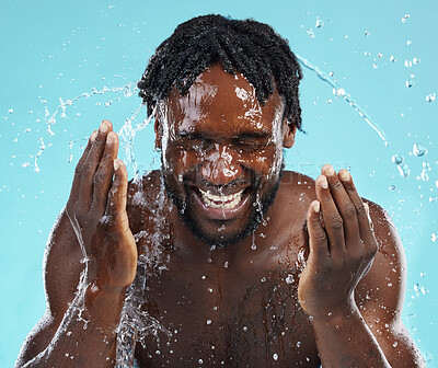 Buy stock photo Water splash, cleaning and face with a model black man in studio on a blue background for hydration. Bathroom, skincare and hygiene with a young male washing his face for natural skin treatment