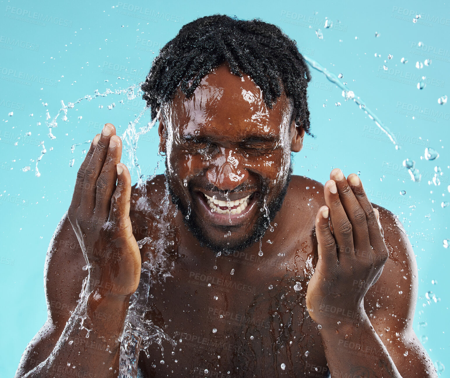 Buy stock photo Water splash, cleaning and face with a model black man in studio on a blue background for hydration. Bathroom, skincare and hygiene with a young male washing his face for natural skin treatment