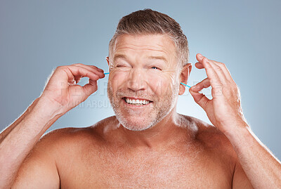 Buy stock photo Earbuds, grooming and man cleaning his ears in a studio for self care, hygiene and cleanliness. Health, wellness and mature guy doing his morning body care routine isolated by a gray background.