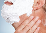 Face, shaving cream and hands of man in studio isolated on a blue background for hair removal. Skincare, cleaning and grooming male model with gel or foam to shave for aesthetics, health and wellness