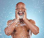 Shower, excited and portrait of a black man with water isolated on a blue background. Cleaning, happy and an African elderly model touching face for skincare and beard grooming on a studio backdrop