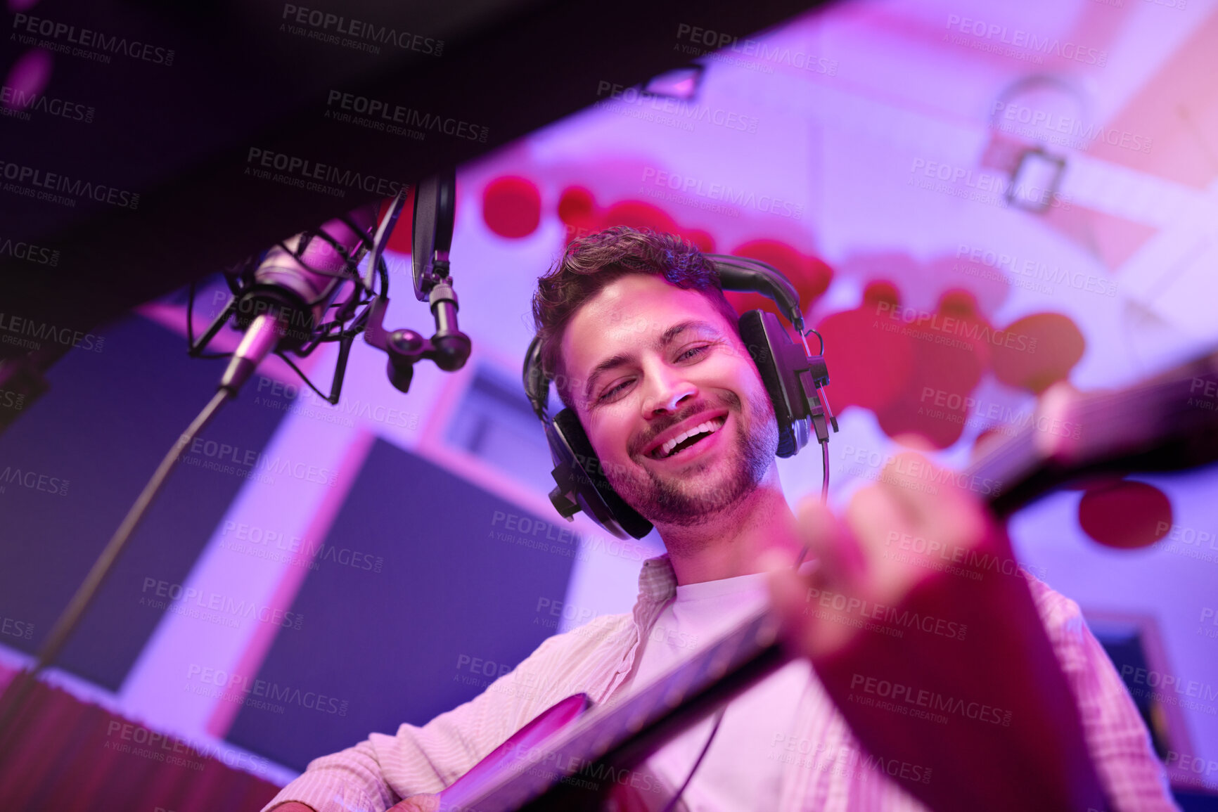 Buy stock photo Happy man, musician or guitar in neon studio, recording production or performance for radio, label or low angle concert. Guitarist, artist or singer playing strings instrument on headphones practice