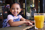 Happy, smile and portrait of a child at a restaurant for food, breakfast and juice. Playful, happiness and girl sitting in a cafe, coffee shop or store for lunch, dinner or meal with a drink