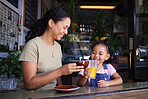 Coffee shop, black family and toast with a mother and daughter enjoying a beverage in a cafe together. Juice, caffeine and cheers with a woman and happy female child bonding in a restaurant