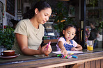 Cafe, family mother and child learning, drawing or color education with support, help and fun at restaurant. Woman or mom with girl kid writing in coffee shop for creativity, teaching and activity