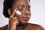 Face, skincare and cream with a model black woman in studio on a gray background for plus size beauty. Eyes closed, skin and lotion with an attractive young female indoor to apply facial treatment