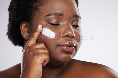 Buy stock photo Face, skincare and cream with a model black woman in studio on a gray background for plus size beauty. Eyes closed, skin and lotion with an attractive young female indoor to apply facial treatment