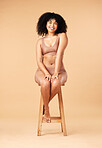 Body, beauty and black woman sitting on a chair for skincare and self care isolated in a studio brown background. Skin, portrait and female model smile, happy and glow due to cosmetic and happiness