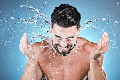 Buy stock photo Water splash, hands and a man model washing his face in studio on a blue background for hygiene or hydration. Bathroom, skincare and cleaning with a handsome young male splashing his skin for beauty