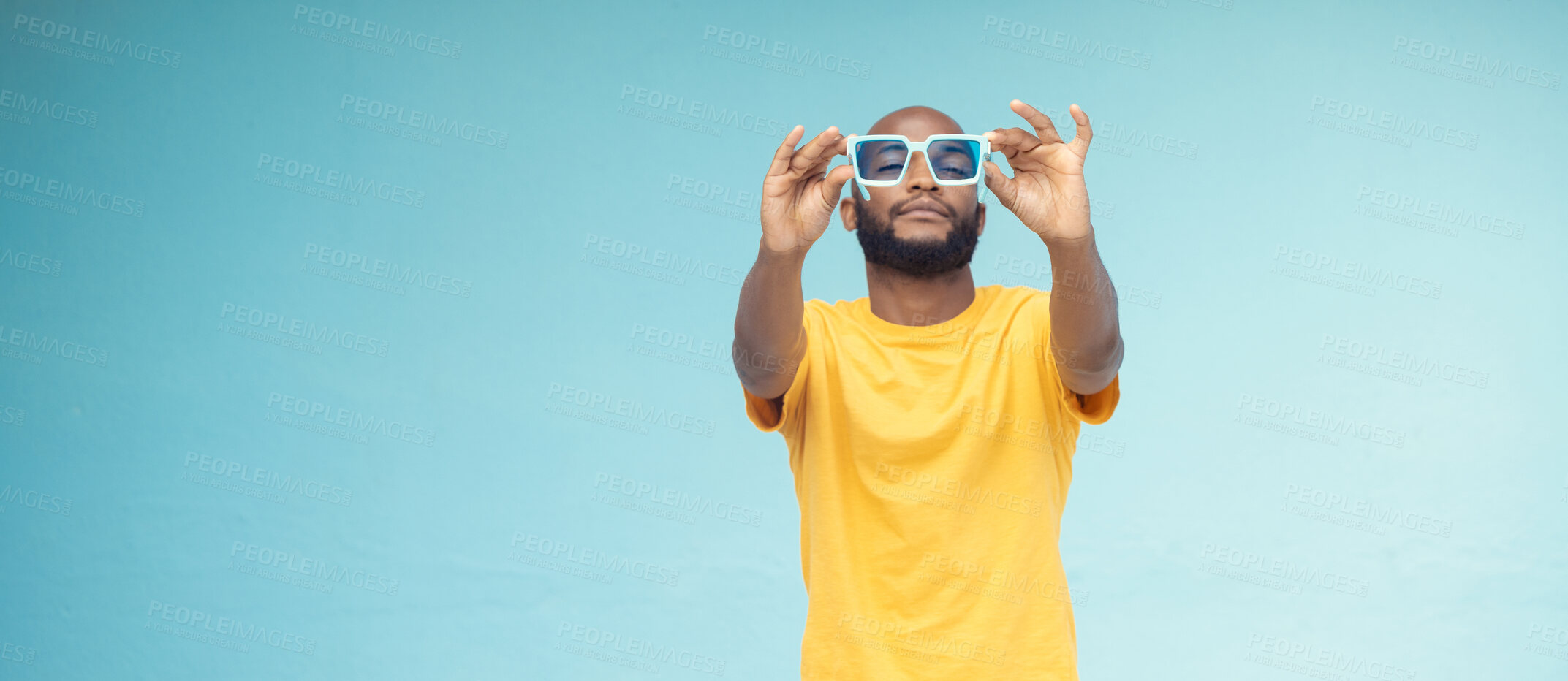 Buy stock photo Black man, sunglasses and fashion on a blue background with cool and trendy style with mock up space. Young model person with eyewear in studio for advertising designer brand, logo or color in hands