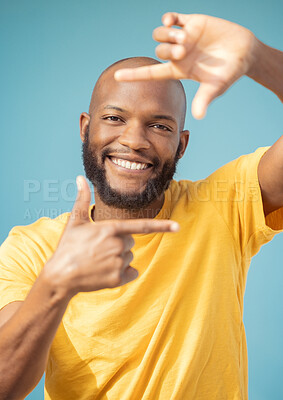 Buy stock photo Hands, frame and portrait of black man on blue background for profile picture. Face, happy guy and finger framing for perspective, selfie and vision of happiness, smile and photography sign in studio