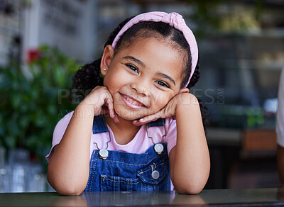 Buy stock photo Black child, face and girl portrait with a smile, happiness and cute clothes with hands for headshot. Happy kid at a table for fashion, positive mindset and blurred background at cafe or home