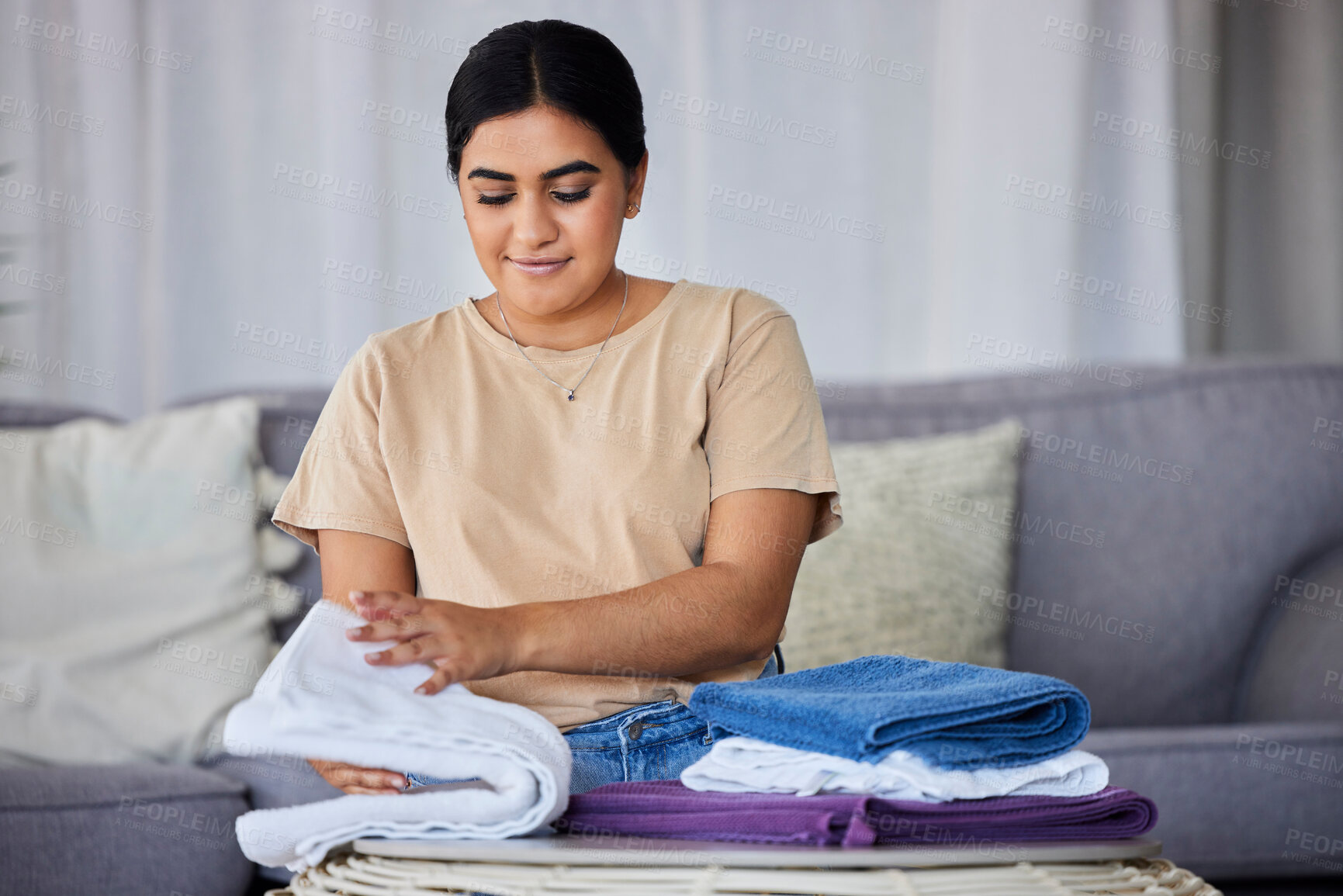 Buy stock photo House, cleaning and woman fold laundry on a sofa, happy and relax alone in her home. Towels, housework and indian female relaxing while sorting fabric, linen and fresh cloth on the weekend or day off