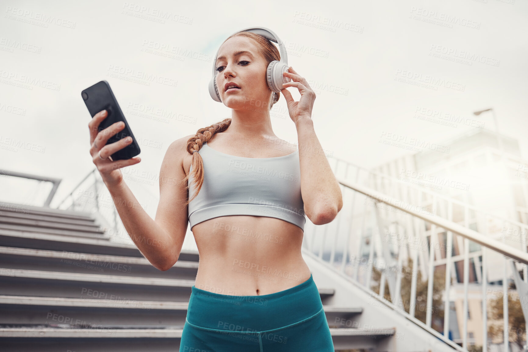 Buy stock photo Woman, runner and phone with headphones for music, radio and web texting on chat app by stairs. Gen z girl, urban workout and fitness with smartphone for networking, social media and internet in city