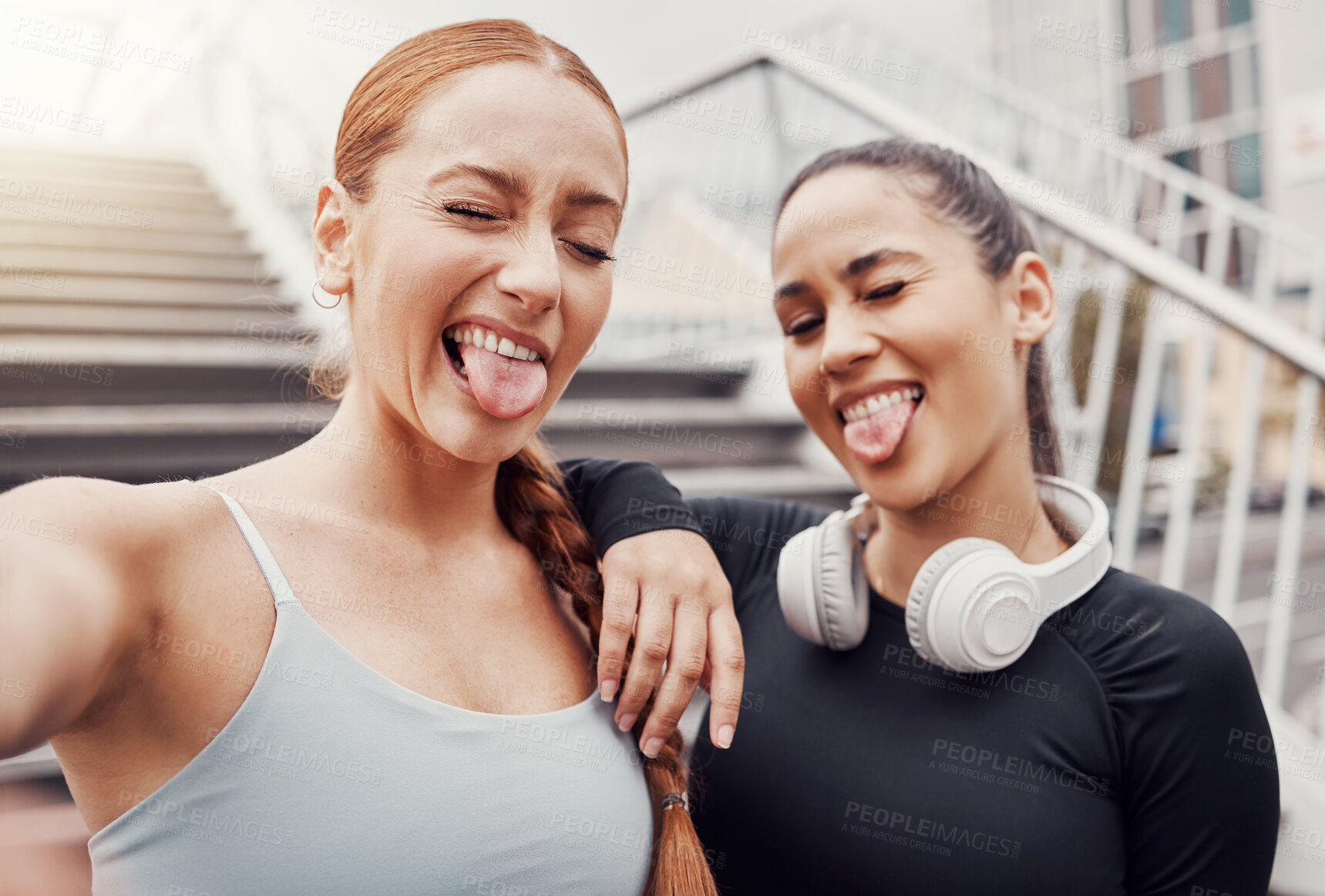 Buy stock photo Women, friends selfie and tongue in city for training, comic time or funny face with headphones in profile picture. Woman workout group, exercise photo or social media by stairs in metro with support