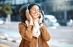 Black woman, music and headphones while happy in city for travel, motivation and mindset. Young person on urban street with buildings background while listening and streaming podcast or audio outdoor