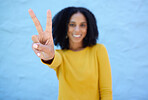 Black woman, hand and peace sign for victory, win or letter V against a blue wall background on mockup. Hand of happy African American female winner smiling showing peaceful symbol, gesture or emoji