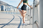 Fitness, woman and stretching legs in the city for running, exercise or cardio workout by the beach. Active female runner in warm up leg stretch preparation for run, exercising or training in nature