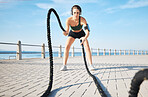 Fitness, woman and battle rope at the beach for intense arm workout, training or endurance exercise. Active female with ropes in power workout, exercising or focus for muscle bodybuilding outdoors