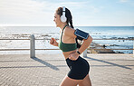 Music, fitness and woman at beach for running, exercise and morning cardio on blue sky background. Radio, podcast and workout run by girl at ocean for training, happy or relax with audio motivation