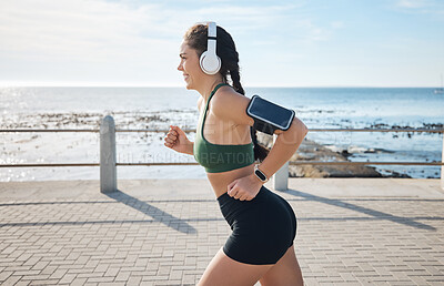 Buy stock photo Music, fitness and woman at beach for running, exercise and morning cardio on blue sky background. Radio, podcast and workout run by girl at ocean for training, happy or relax with audio motivation