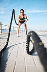 Fitness, woman and battle rope for intense arm workout, training or endurance exercise at the beach. Active female with ropes in power workout, exercising or focus for muscle bodybuilding outdoors