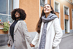 Woman, friends and holding hands walking in the city for friendship, travel or fun journey in the outdoors. Happy women taking walk or stroll touching hand with smile for sightseeing in an urban town