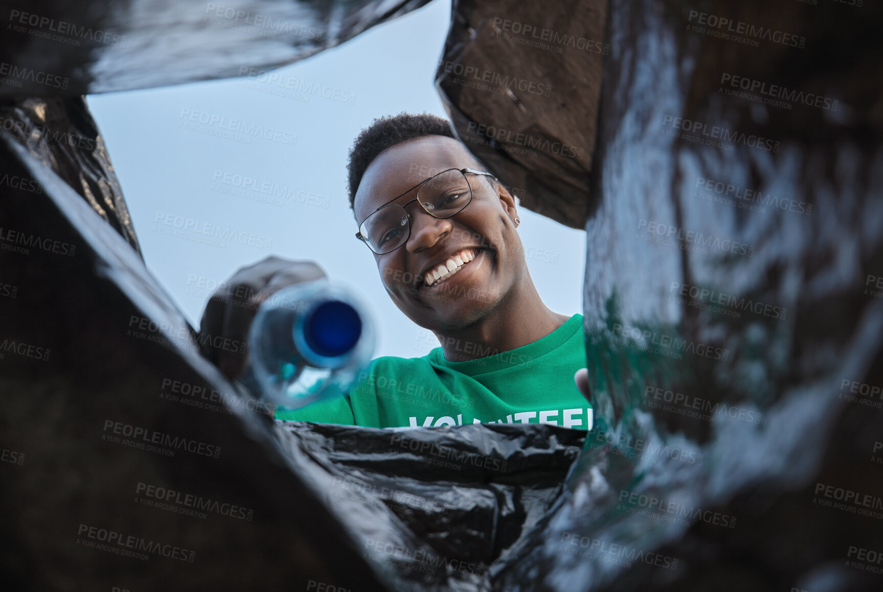 Buy stock photo Recycle, smile and black man with view in bag, sustainability and cleaning plastic pollution, earth day and help in community. Saving the environment, charity and people putting trash in garbage bin.