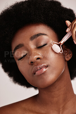 Buy stock photo Black woman, skin care and facial roller for face massage in studio with dermatology and cosmetic tools. Aesthetic model with hands for spa product for health, wellness and natural youth skin glow 