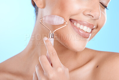 Buy stock photo Skincare, massage and woman with face roller in studio for beauty, wellness and anti aging treatment on blue background, Facial, happy and girl model relax with rose quartz product and isolated