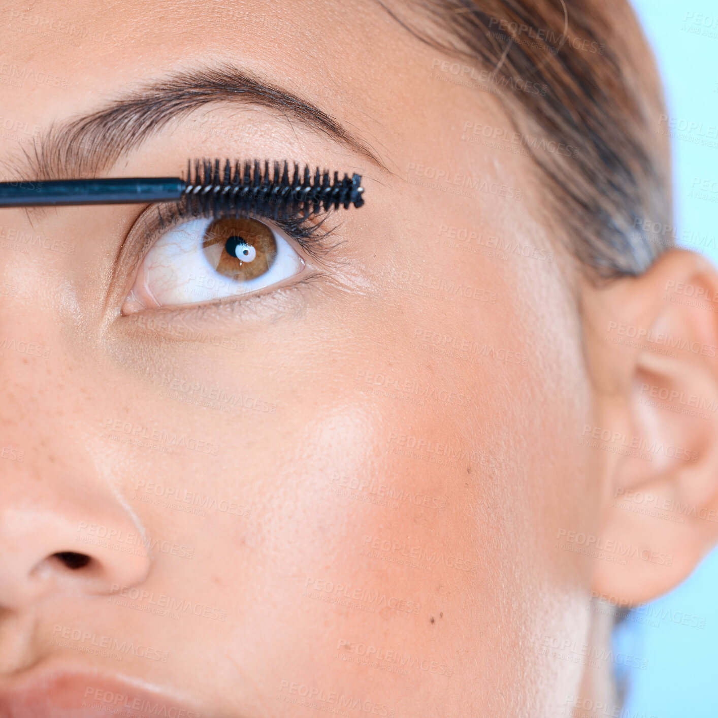 Buy stock photo Makeup, mascara and eyelashes with a black woman in studio on a blue background for beauty. Eyes, cosmetics and zoom with an attractive young female model closeup to apply a cosmetic product