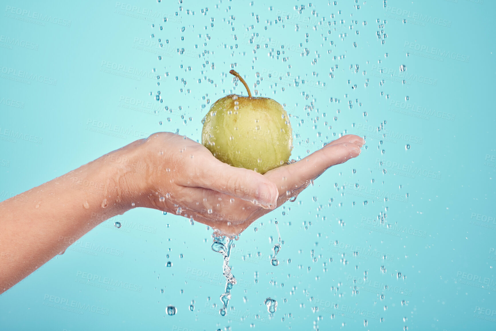 Buy stock photo Water splash, cleaning and hands with apple in studio isolated on a blue background. Nutritionist, fruits and model or woman washing food for healthy diet, vitamin c or skincare, beauty or wellness.