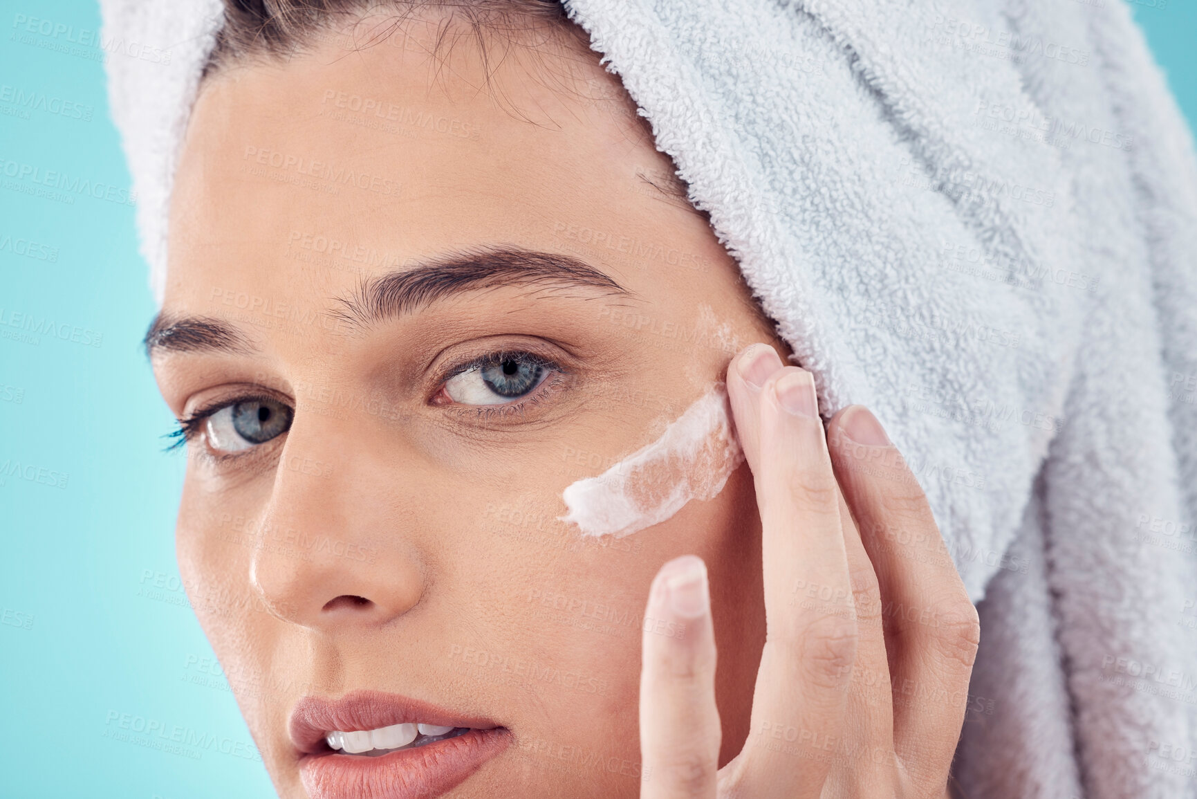 Buy stock photo Towel, face and woman with skincare cream in studio isolated on a blue background. Portrait, dermatology and young female model apply lotion cosmetics, creme or facial moisturizer for healthy skin.