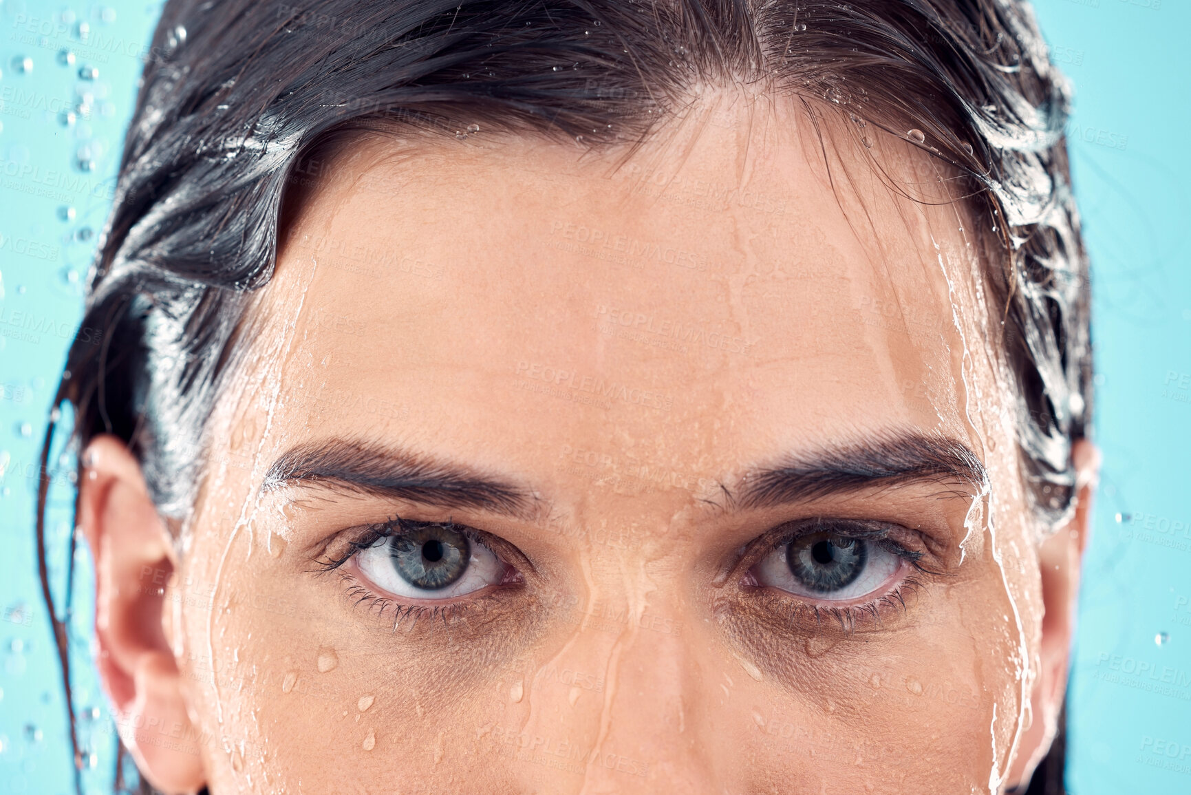 Buy stock photo Water splash, skincare and eyes of woman in shower in studio isolated on a blue background. Beauty, face portrait and young female model washing, cleaning or bathing for hygiene, wellness and health.