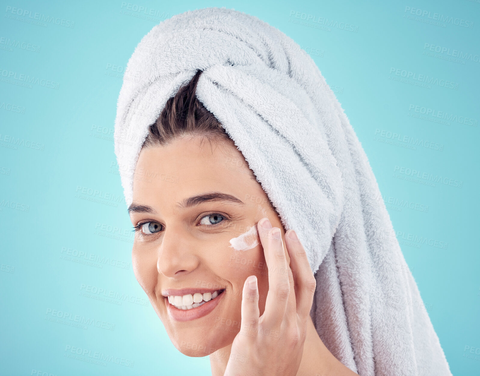 Buy stock photo Face, towel and woman with skincare cream in studio isolated on a blue background. Portrait, dermatology and happy female model apply lotion cosmetics, creme or facial moisturizer for healthy skin.