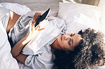 Black woman, bed and phone in home bedroom for social media, texting or internet browsing in the morning. Technology, relax and female with mobile smartphone for web scrolling or networking in house.