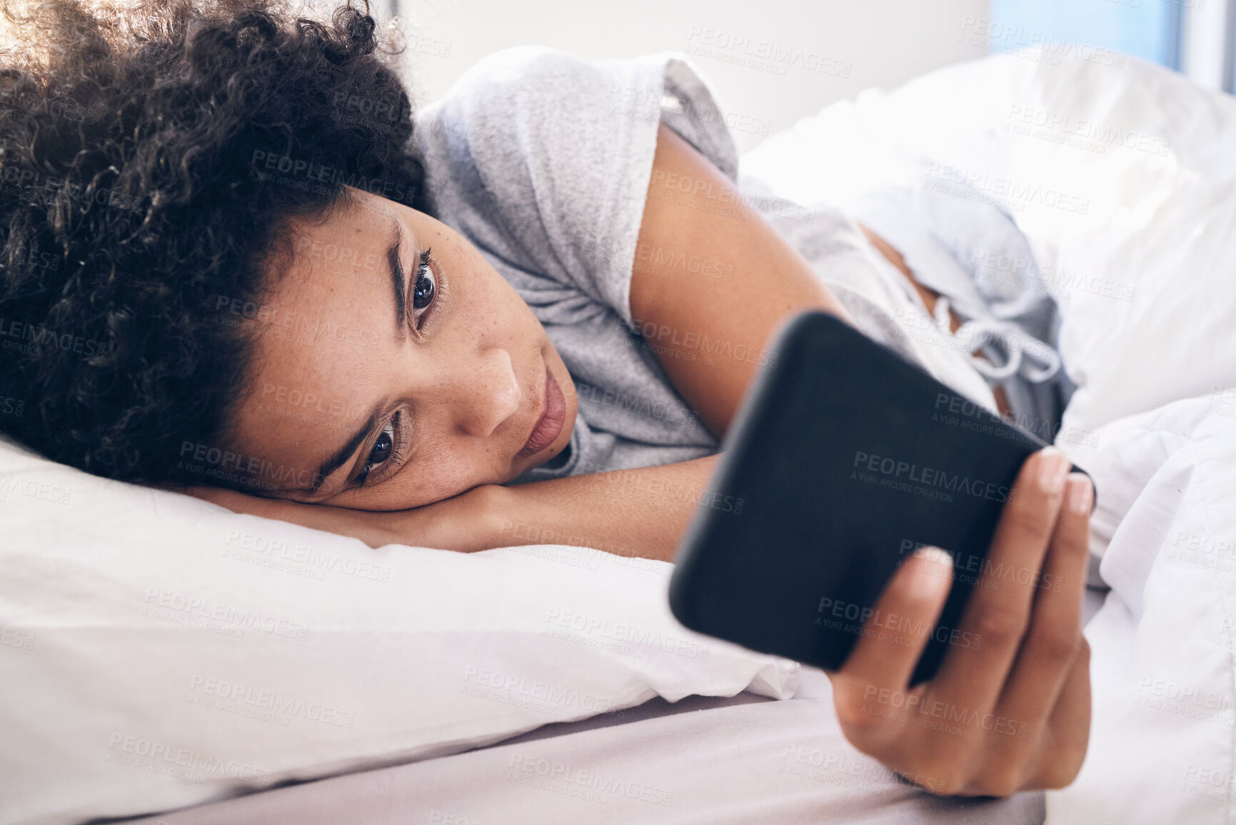 Buy stock photo Phone, social media and a black woman lying in bed in the morning after waking up on the weekend. Mobile, communication and relax with an attractive young female resting in her bedroom in a house