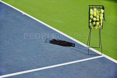 Tennis, sport balls and basket of sports equipment on a training court outdoor with no people. Exercise, fitness and workout equipment shadow for match of game competition on turf ground in summer