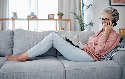Buy stock photo Phone call, reading and relax on the sofa with a senior woman in the living room of her home over the weekend. Mobile, books and retirement with a mature female sitting on a couch in the lounge