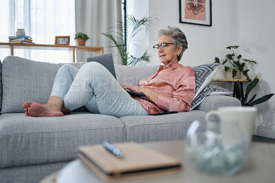 Buy stock photo Senior woman, laptop and relax on sofa in the living room checking email, typing or writing at home. Elderly female freelancer or writer relaxing on lounge couch working or reading on computer